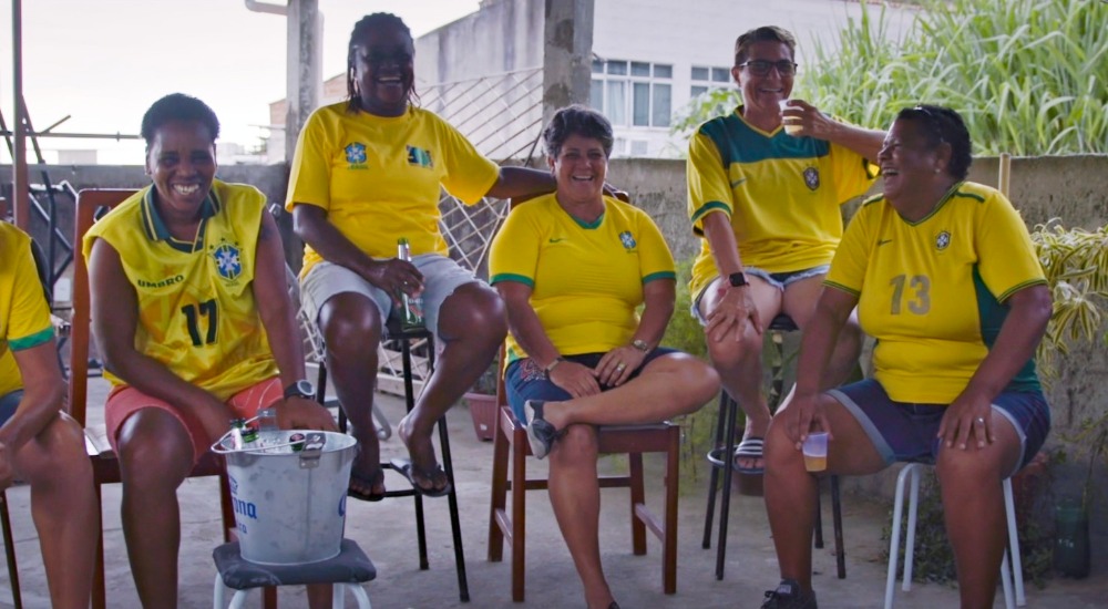 A group of women sit for a photo in Brazilian soccer jerseys.