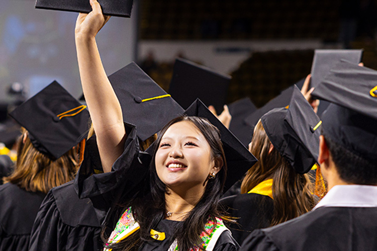 A graduate raises her cap in a crowd at commencement.