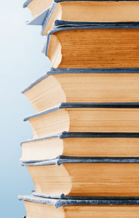 Multiple books stacked on top of each other. Every book has a denim-blue cover and the pages have been sun bleached over time.