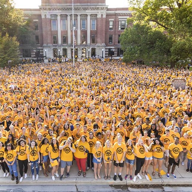 Numerous FPM employees are all gathered together. They are all in yellow shirts standing together in front of Mitchell Hall.