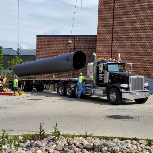Large black, metal chimney being lowered onto a large semi truck flatbed