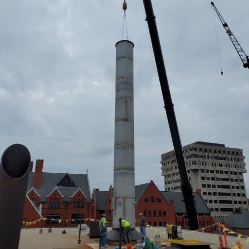 Rooftop image of 3-person construction crew guiding a gray smokestack into place
