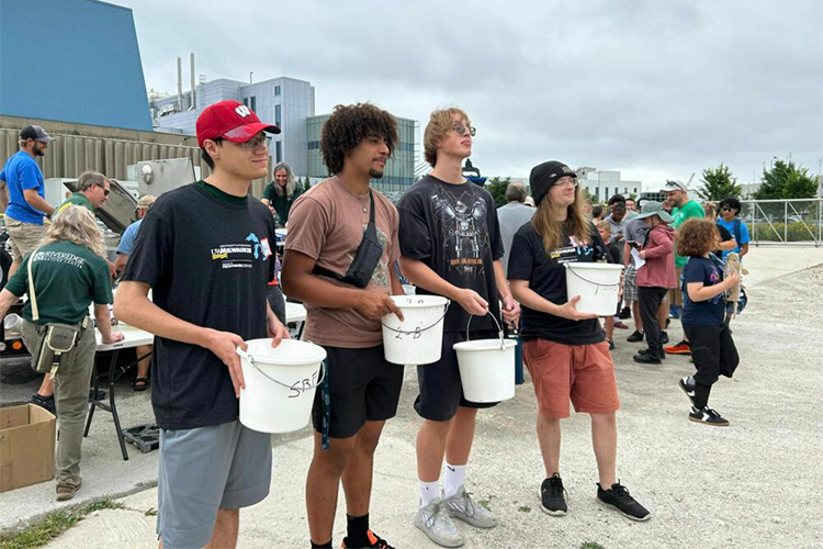 Four attendees of Sturgeon Fest carry buckets with baby sturgeon in them to release into the harbor.