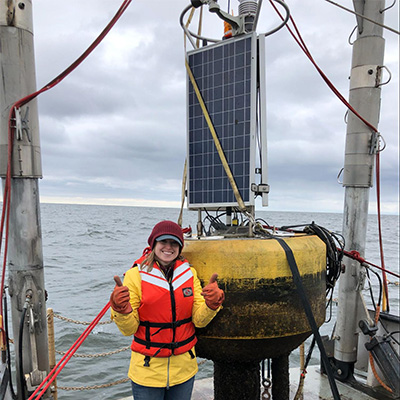 A woman with a large buoy and the water behind on an overcast day.