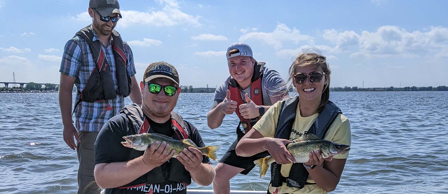 Students on a boat holding fish in their hands.