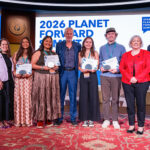 A group of people are in a line holding awards with a digital screen behind them.