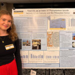 A woman stands next to a research poster.