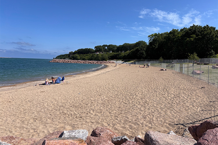 Sand beach with rocks in the foreground and blue water.