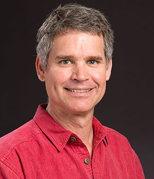 John Berges smiling against a dark background.
