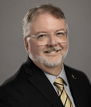 Bryan Porter smiles in front of a gray background.