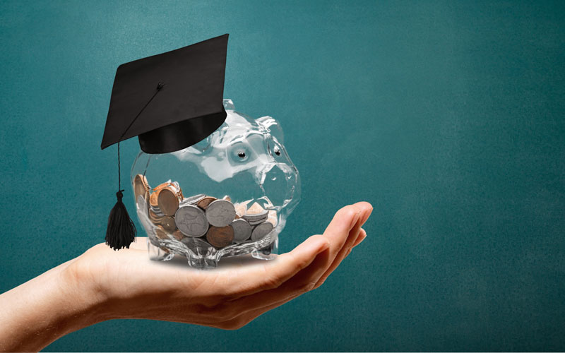 hand holding piggy bank with graduation cap on top