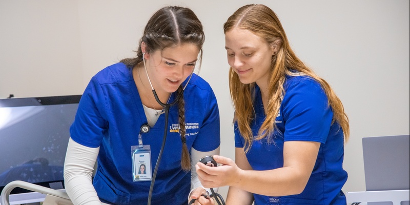 Nursing students in scrubs looking at a simulated patients blood pressure.