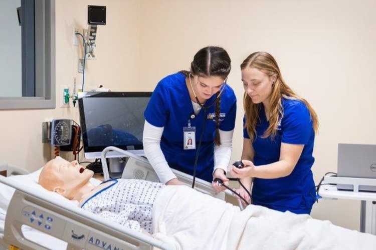 Two Nursing students check the blood pressure of a simulated patient.