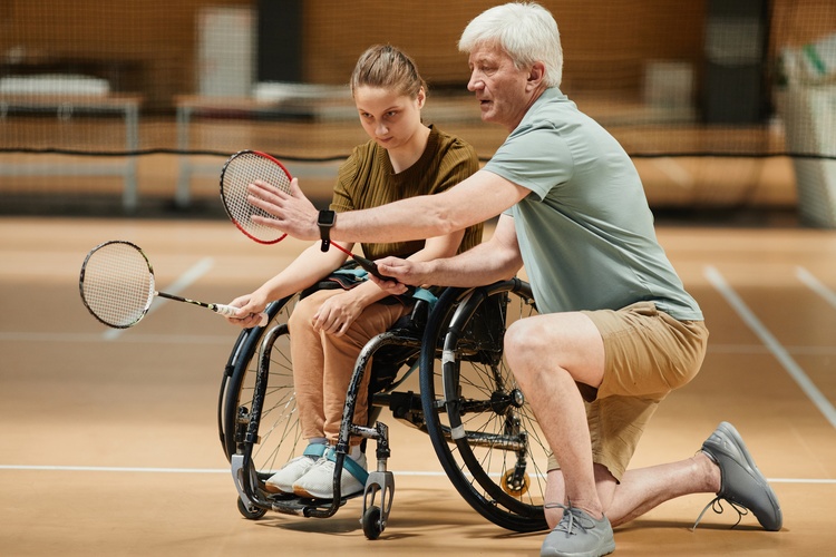 A Recreation Therapist teaches a student who uses a wheelchair how to play badminton.