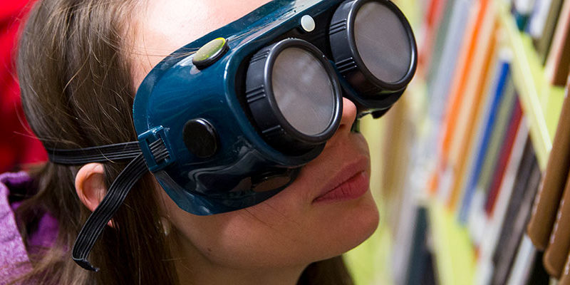 Occupational Studies student wears goggles that simulate visual impairment while finding a library book.