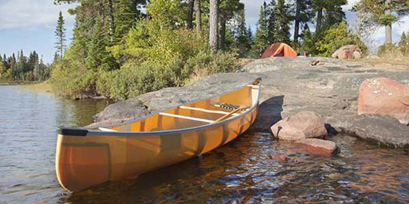 Campsite and canoe on rocky shore of lake.