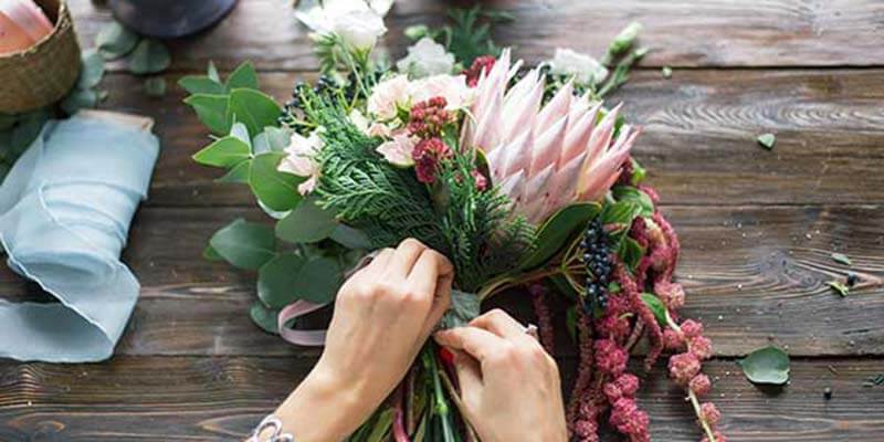 Hand tying a ribbon on a bouquet of flowers.