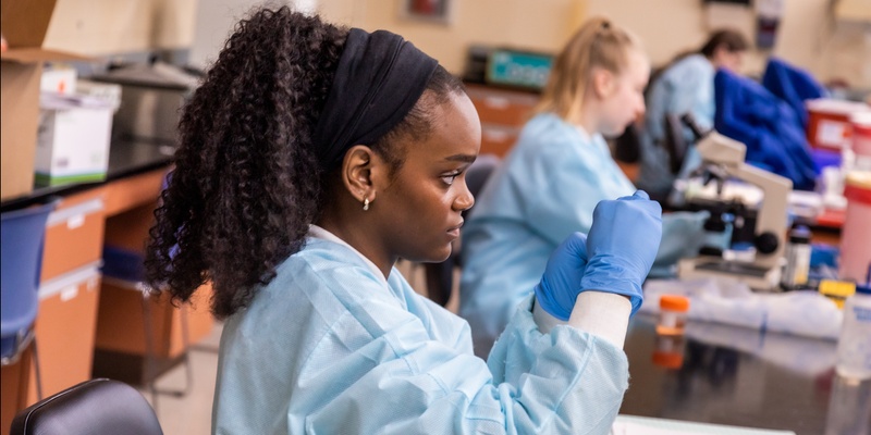 African American woman working on a laboratory test whole wearing gloves and lab coat.