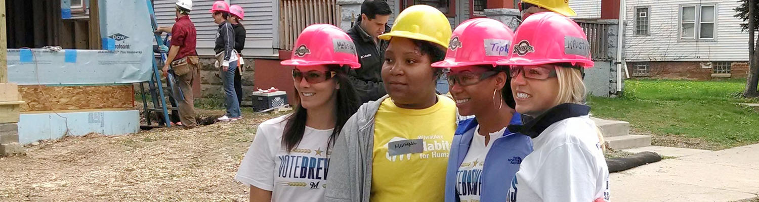 Four volunteers in hard hats smile at a Milwaukee Habitat for Humanity construction site.