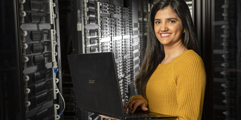 Female undergraduate student holding laptop while working in server room