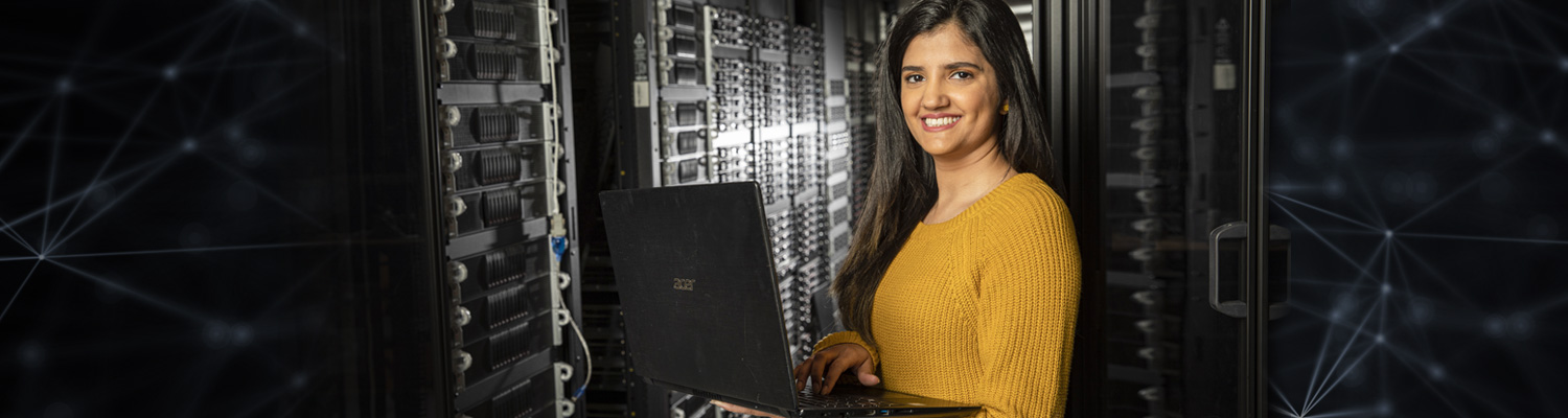 Female undergraduate student holding laptop while working in server room