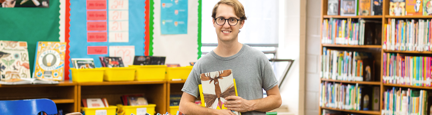 Male student holding books while working in an elementary school library environment