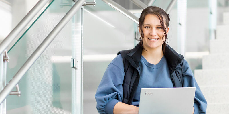 Information Science & Technology student smiling at camera while sitting on staircase with laptop.