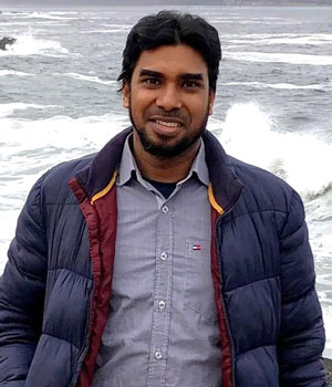 Front-facing portrait of PhD student Rory Wahab. He is standing in front of a body of water, smiling, with a blue winter jacket.