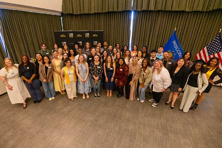 Spring 2026 Graduates standing in front of a black and gold banner that says UWM Proud. Spring 2026 Graduates standing in front of a black and gold banner that says UWM Proud.