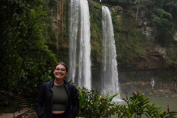 A UWM student poses in front of a jungle waterfall 
