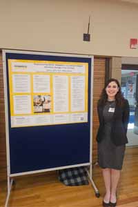 Rivka Comrov stands next to a yellow and white poster displaying the results of her research