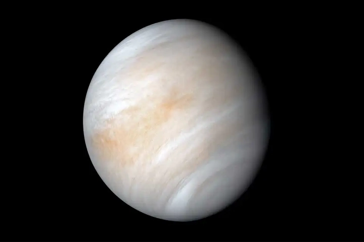 The planet Venus against a black background. The planet is covered in yellow, pale orange, and white swirls.