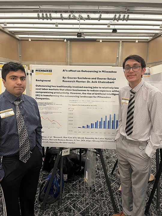 Two southeast Asian young men wearing business casual clothing stand in front of a white poster with black writing and a blue bar graph.
