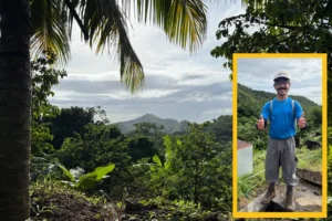 A layered image. The background image is a lush rain forest landscape with a mountain in the distance. An offset image in the bottom right corner is a young man with a black mustache wearing a ball cap, blue shirt, cargo pants, and boots. He flashes a double thumbs-up at the viewer.