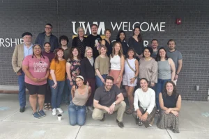A large group of young to middle-aged people smile at the camera in front of a sign that reads UWM Welcome.