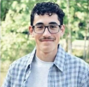 A headshot of a young man with glasses and dark curly hair wearing a collared shirt.