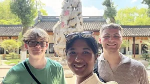 Three students take a selfie in front of a Chinese building on a sunny day