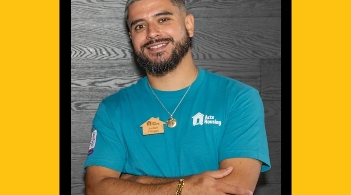 A headshot of a Hispanic man with short dark hair wearing a teal t-shirt with an Acts Housing logo.