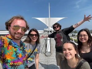 A group of five graduate and undergraduate students take a selfie on the bridge leading to the Calatrava at the Milwaukee Art Museum.