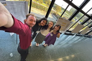 Four students take a selfie in front a research poster