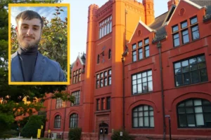 A headshot of young white man with a beard is overlaid on am image of Merrill Hall, a red brick building with numerous glass windows.