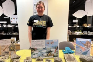 A young woman stands behind a table covered in fossils and displays about the Silurian Sea.