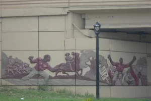 A mural on the side of a highway. The mural depicts an uprising rescuing an enslaved man from jail.