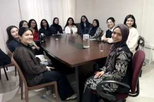 A group of young southeast Asian women sit around a conference table and smile at the viewer.