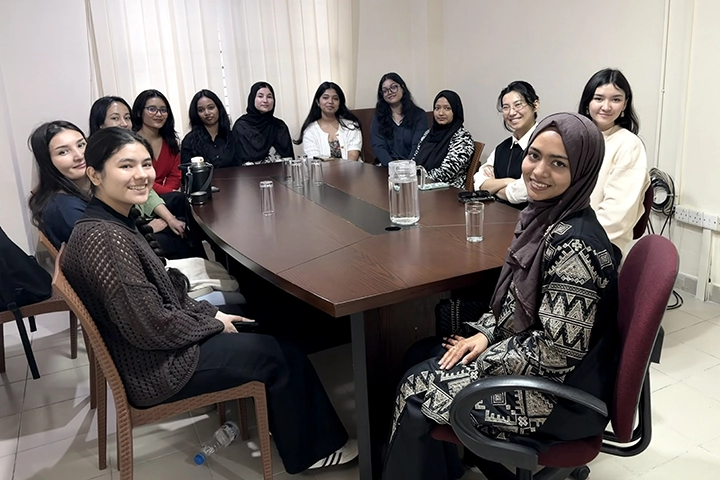 A group of young southeast Asian women sit around a conference table and smile at the viewer.