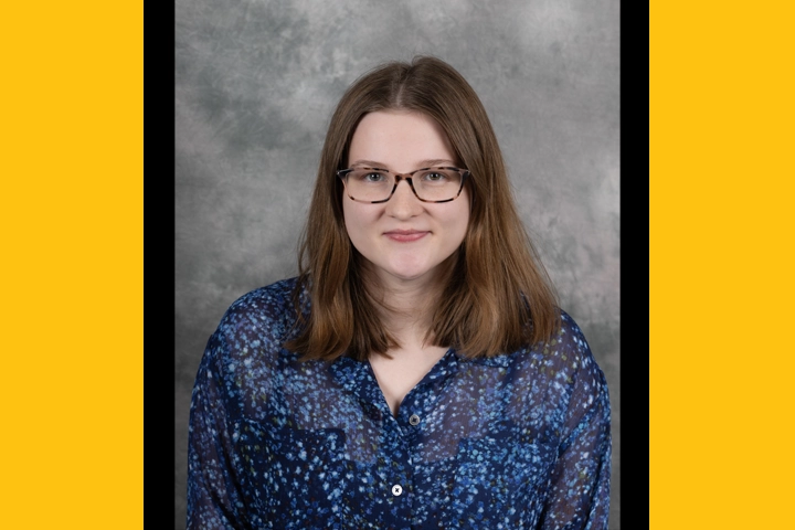 Headshot of a young white woman with brown hair wearing glasses and a blue blouse.