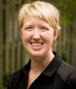 Headshot of a white woman with a blond pixie cut, smiling at the viewer.