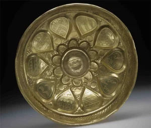 The inside of a metal drinking cup is shown engraved with images of heraldic shields.