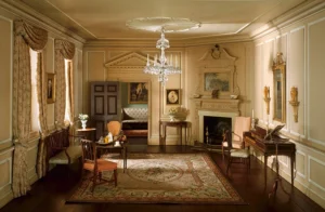 A Thorne miniature room, showing crown molding, wood floors, a throw rug, fireplace, desk and chairs, and other decor of an upper-middle class room.