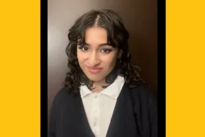 A headshot of a young Latina woman with curly dark hair, wearing a collared shirt and black cardigan.